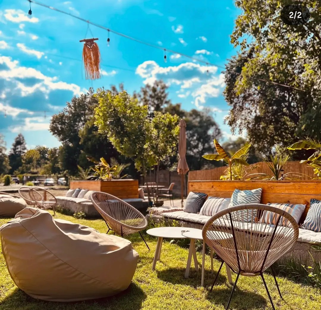 Terasa August Lounge ziua, cu scaune de răchită, jardiniere de lemn și cer senin