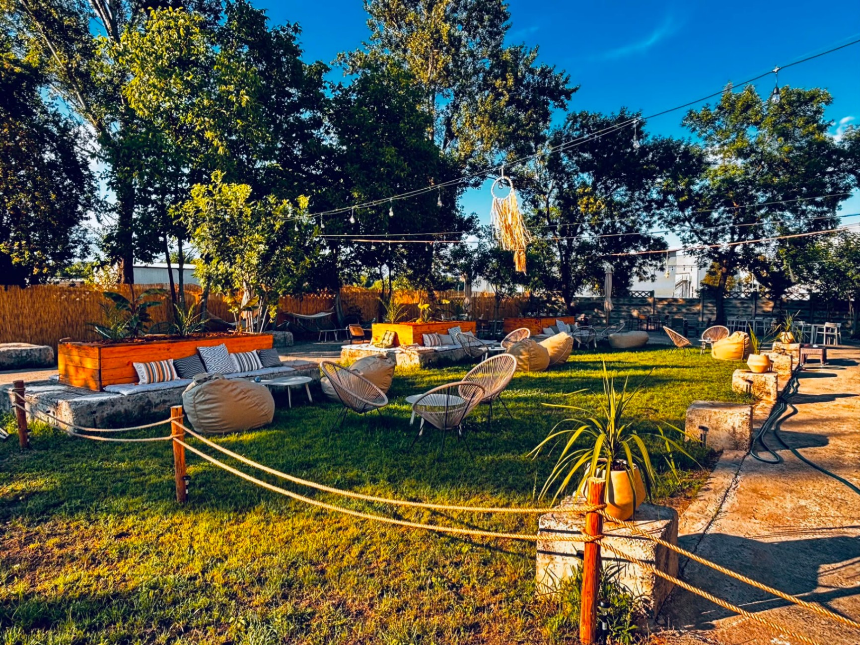 Terasa August Lounge ziua, cu scaune de răchită, jardiniere de lemn și cer senin